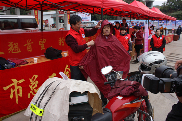 梧州市總工會(huì)的黨員義工們?cè)谑袞|出口春運(yùn)服務(wù)站助力“摩托大軍”平安返鄉(xiāng)，幫助他們檢查車輛和行李，穿上雨衣。--黃賀峰攝.j